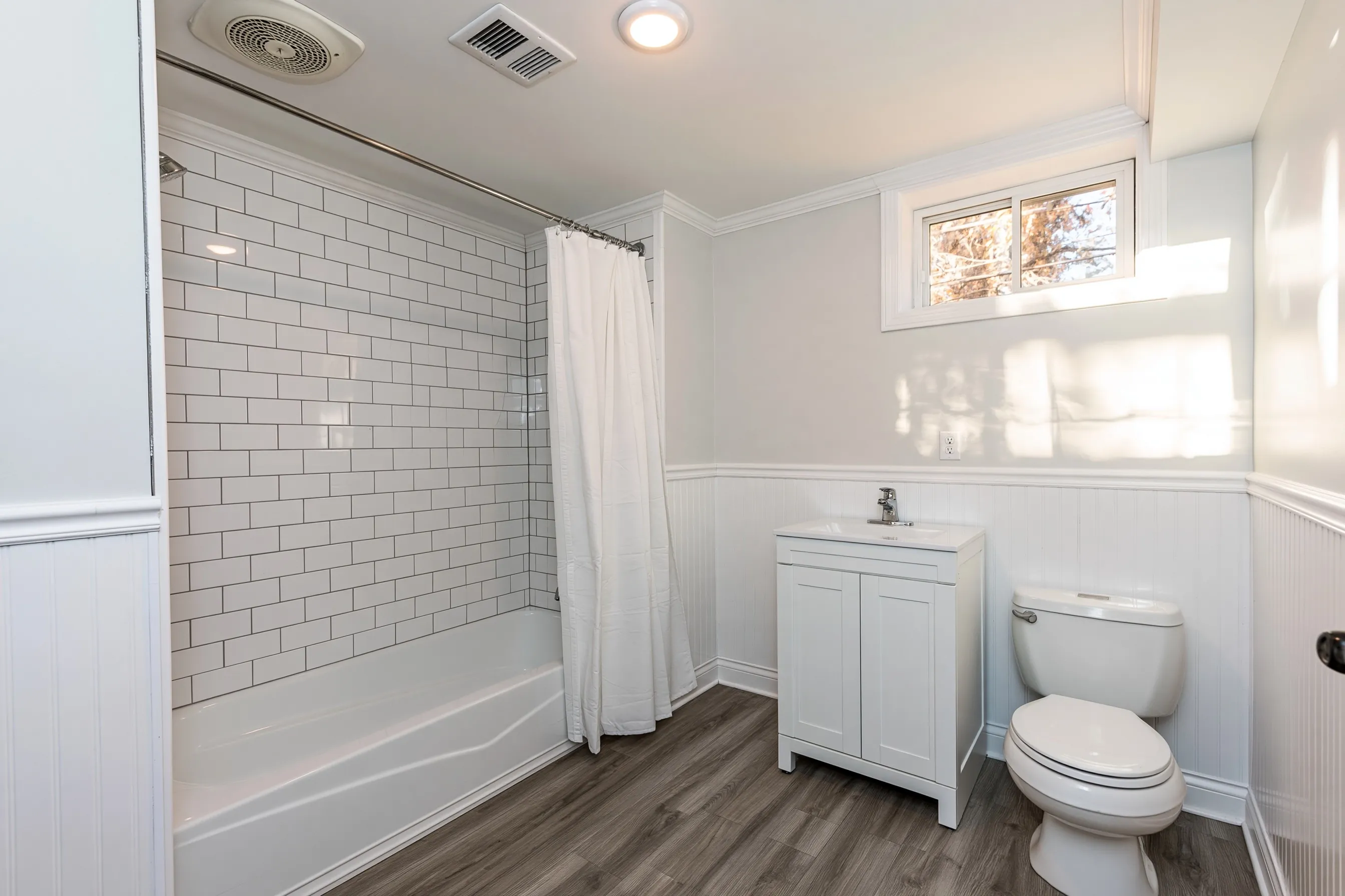 Finished basement bathroom with a tub-and-shower combination, white subway tile, a vanity and a small high window